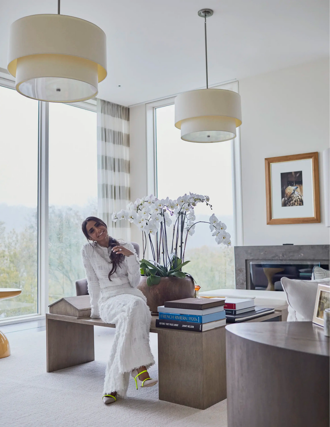 Abeer Al Otaiba in a white pantsuit, sitting on a desk in her office.